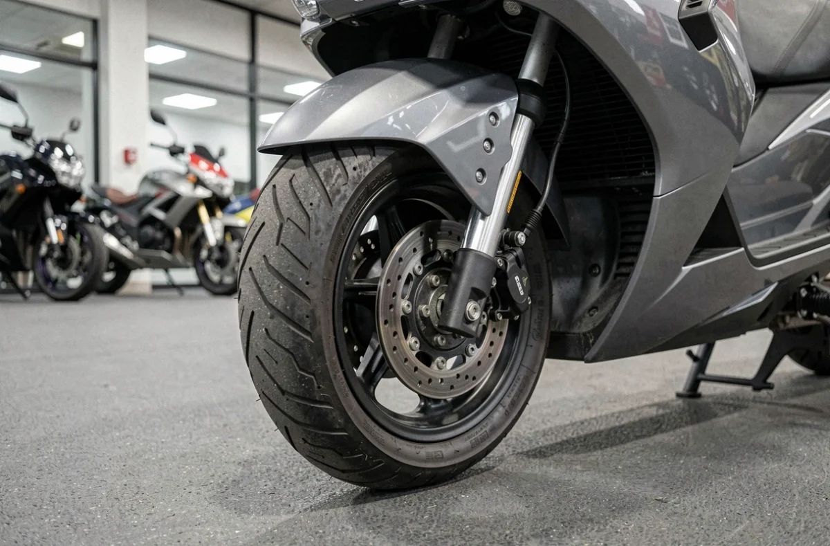 Détail du train avant d'un trois-roues motorisé dans une concession, mettant en valeur la mécanique spécifique aux motos trois roues
